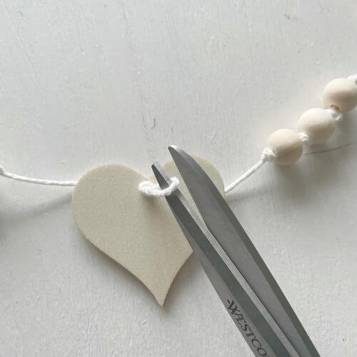 Cut excess string from knot on wood heart