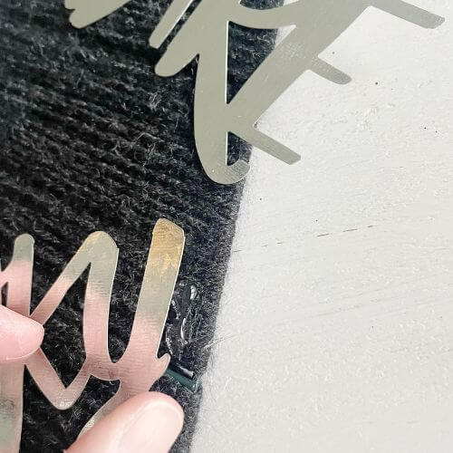 Hot glue metal letters by lifting them up and placing glue beneath them
