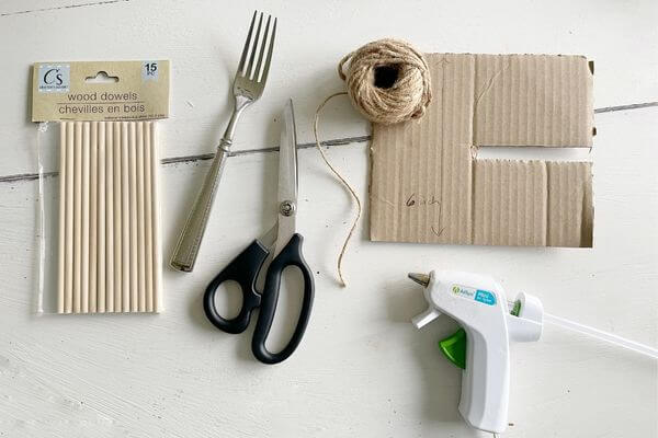 Supplies including dowel rods, fork, scissors, twine, cardboard and glue gun.