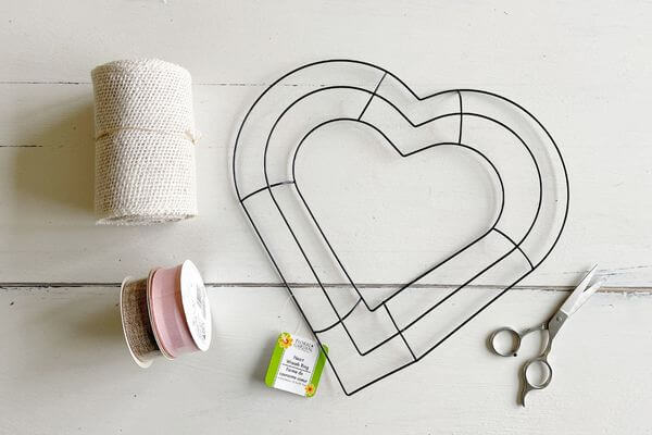Supplies including heart wreath form, burlap, scissors, and 2 rolls of ribbons (brown and pink)