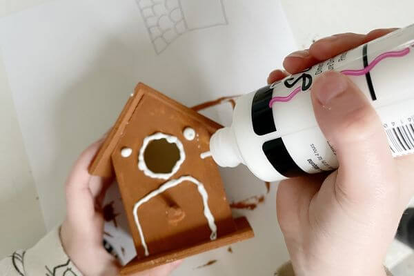 Painting designs on the birdhouse with white dimensional fabric paint