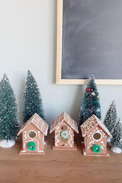 Three gingerbread painted wooden birdhouses sitting amongst bottle brush trees.