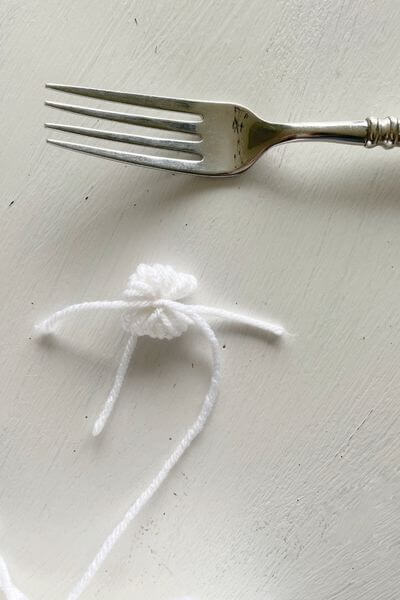 Slide the pom pom off the fork, tie it tighter and make a knot.