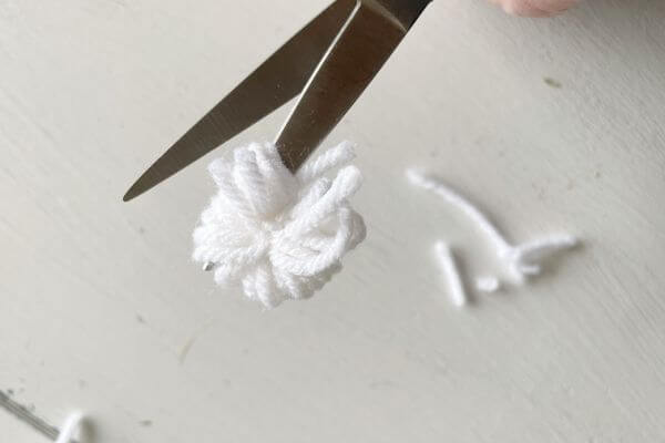 After sliding the yarn off the fork, cut one side of the pom pom with scissors.