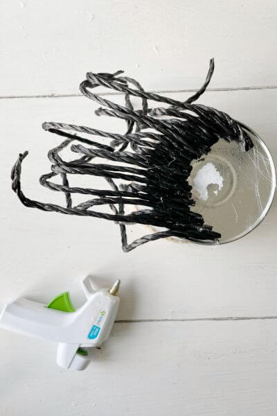 Hot glue twenty 7-inch black poly rope strands onto the bottom of the galvanized vase toward the front of the gnome. 
