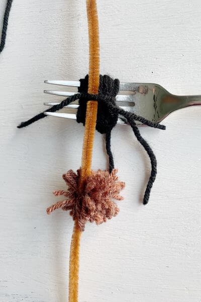 Loop the black yarn 30 times around the fork, and then using another piece of string tie it to the fuzzy stick.