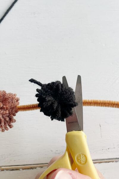 Clip around the yarn ball with the scissors to create the black pom-pom.