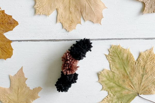 Woolly bear caterpillar made out of pom-poms surrounded by fall leaves.
