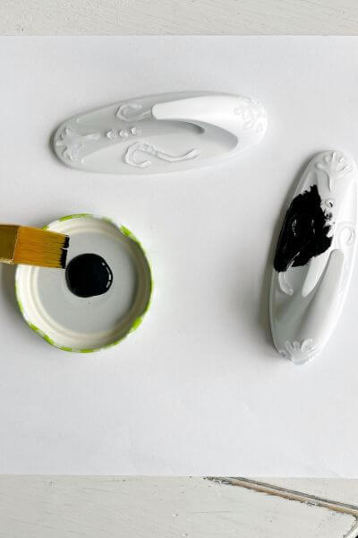 Two white command hooks with a craft paintbrush and black paint in a dish. 