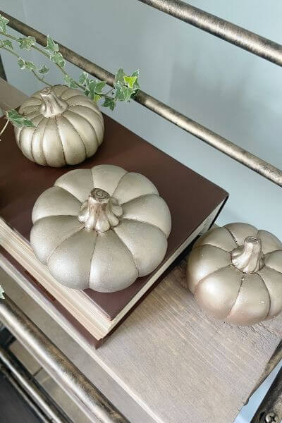 Three gold pumpkins displayed on a shelf.