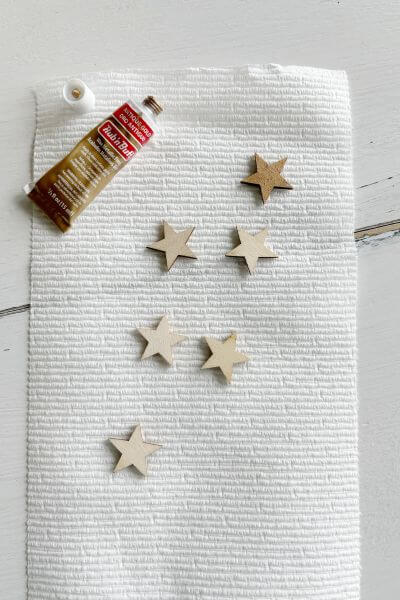 6 wood stars on a paper towel with Rub n' Buff applied to one of them. 