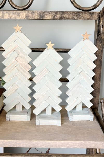 Three green paint washed wooden Jenga block trees with gold stars on top. 
