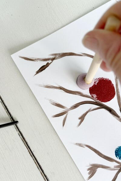 Using craft sponge to create a red bird on the painted tree. 