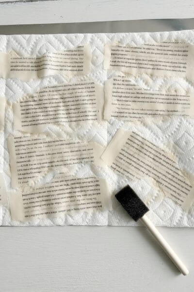 Torn book pages on paper towel with craft sponge brush nearby.