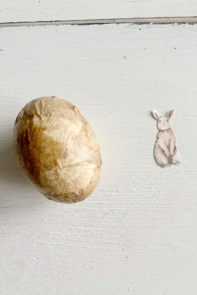 Decoupaged egg sitting next to rabbit cut-out. 