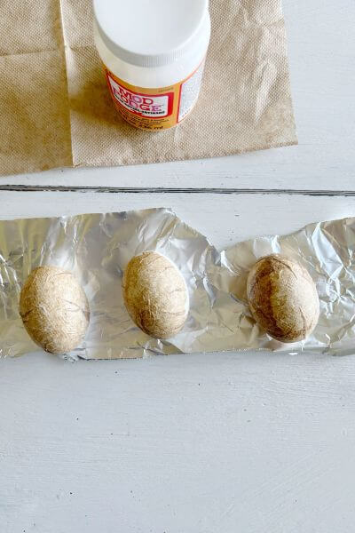 Three eggs decoupaged with brown paper napkins sitting on tin foil. 