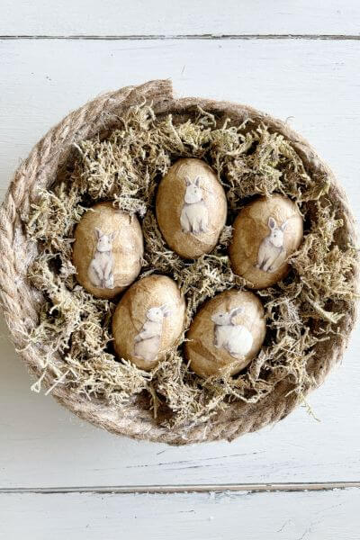 Five decoupaged eggs with rabbit cut-outs sitting in a jute rope nest.
