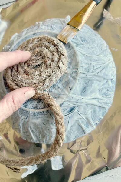 Bottom of bowl with jute rope almost covering it. Paintbrush applying mod podge. 