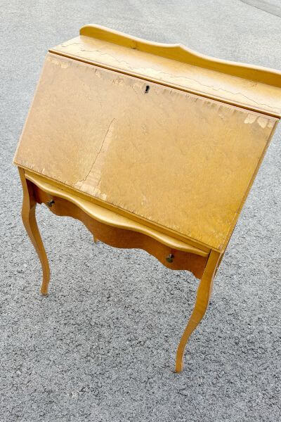 Thrifted secretary's desk with cracked veneer sitting on pavement.