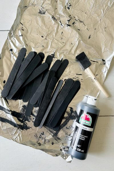 Craft sticks painted black sitting on tin foil.