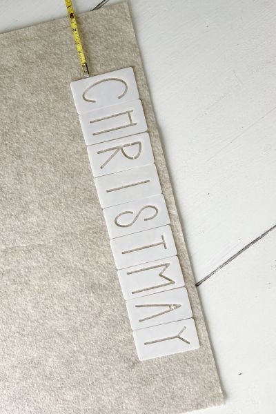 Stencils saying "Christmas" lined up on sandstone colored felt. 