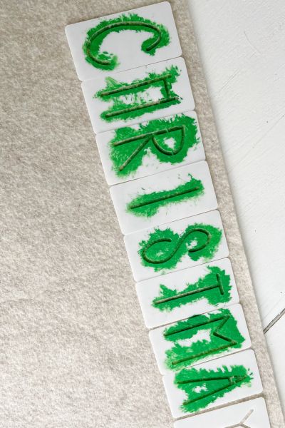 Green paint applied to the felt using the stencils to say the word Christmas. 