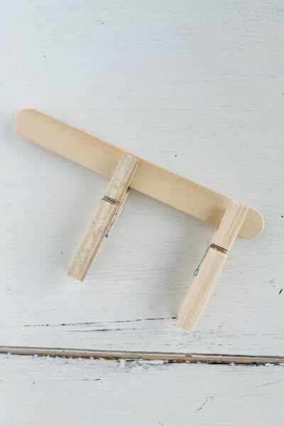 Large popsicle stick with two clothespins pinned to it. 