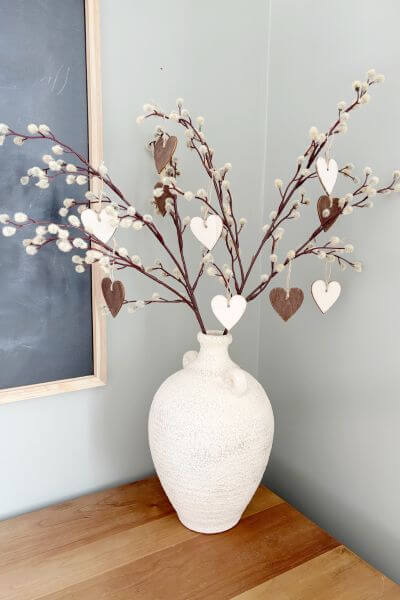 Wood heart ornaments in a white vase hanging on pussy willow branches. 