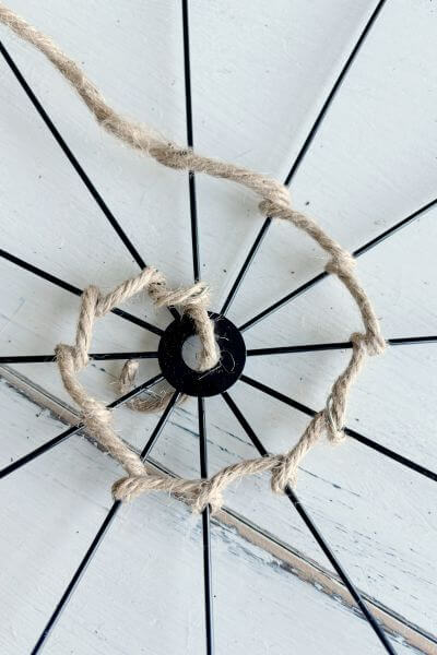 Forming a spider's web using jute wire and wrapping it around the spokes of a bicycle wheel wreath form. 