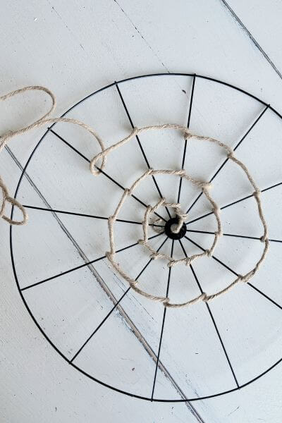 Jute wire being wrapped inside the spokes of a bicycle wheel wreath form to look like a web.
