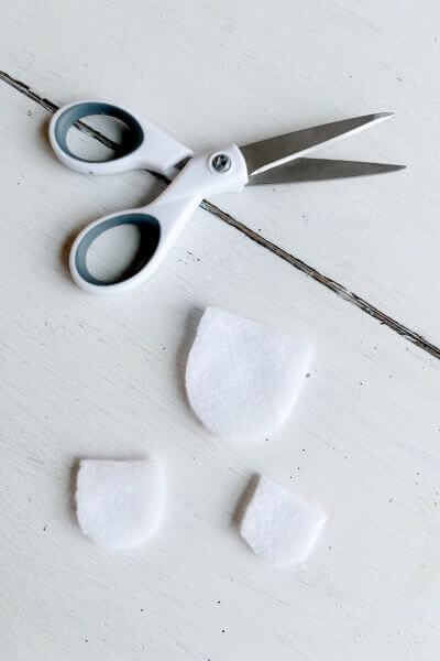 Three pieces of white felt cut out to make the angels' dresses. 