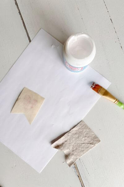 Fabric mod podge, paper printable, paintbrush and drop cloth piece on a table.