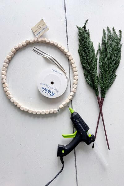 Supplies including wood bead wreath, evergreen pics, glue gun and ribbon.