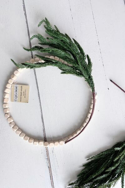 Evergreen pic stem bent in the shape of the wood bead wreath.