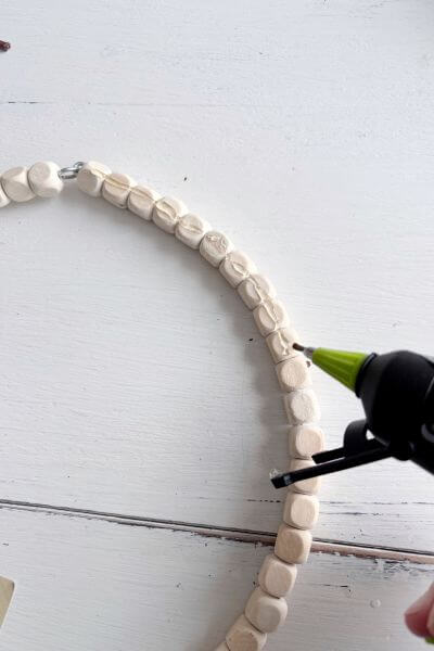 Place hot glue along the wood bead wreath to glue the stem of the first evergreen pic.