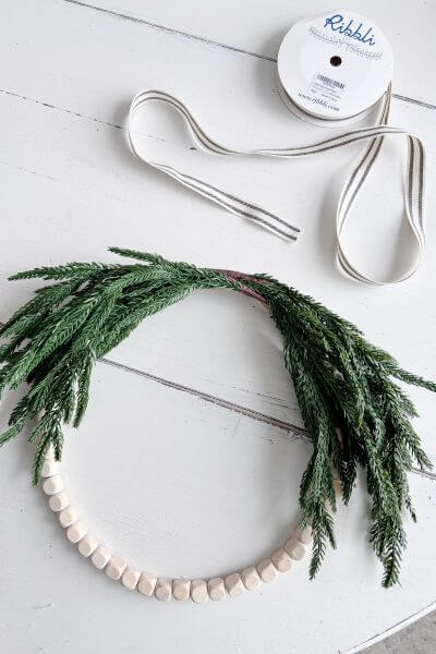 Farmhouse style ribbon sitting near the wood bead evergreen wreath.